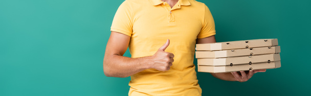 cropped view of delivery man holding pizza boxes and showing thumb up on blue, banner - Foto, Bild
