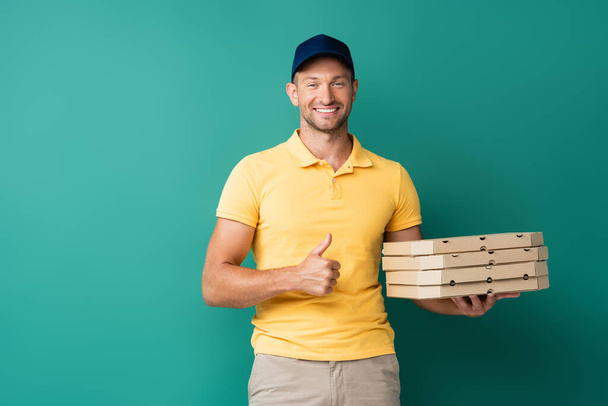 szczęśliwy dostawca trzyma pudełka po pizzy i pokazuje kciuk w górę na niebieski - Zdjęcie, obraz