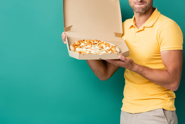 corte vista de entrega homem mordendo lábios enquanto segurando pizza saborosa na caixa em azul - Foto, Imagem