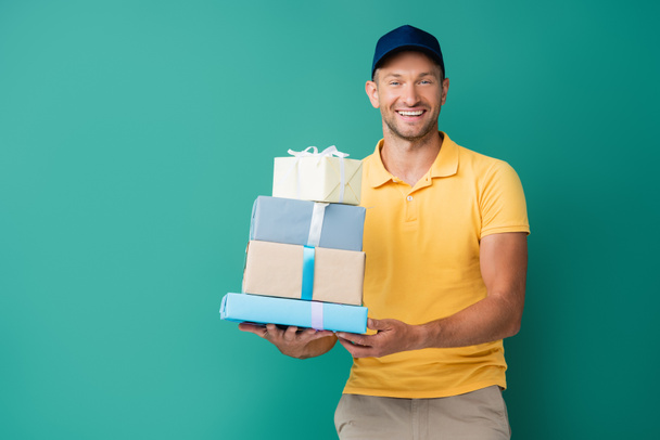 усміхнений чоловік доставки в кепці тримає загорнуті подарунки на синьому
 - Фото, зображення
