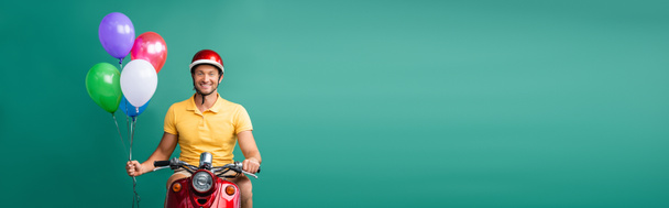 счастливый роженица в шлеме ездит на скутере, держа в руках воздушные шары синего цвета, баннер - Фото, изображение