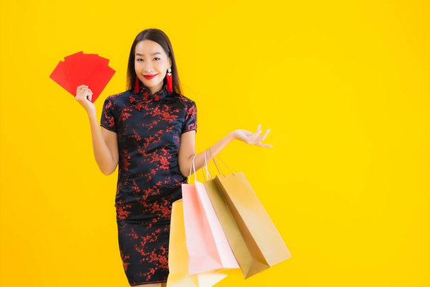 Портрет красивая молодая азиатская женщина носить китайское платье с сумкой, смартфон, кредитная карта для китайского нового года на желтом изолированном фоне
 - Фото, изображение