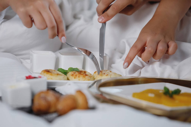 Bearded man and a woman in white coats are having breakfast in bed. Selective focus. Clouse-up. - Foto, imagen
