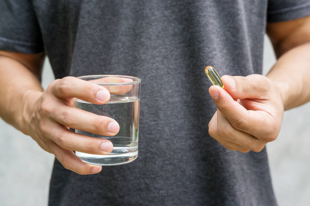 Close up of a man holding a fish oil capsule and a glass of water. - Photo, Image