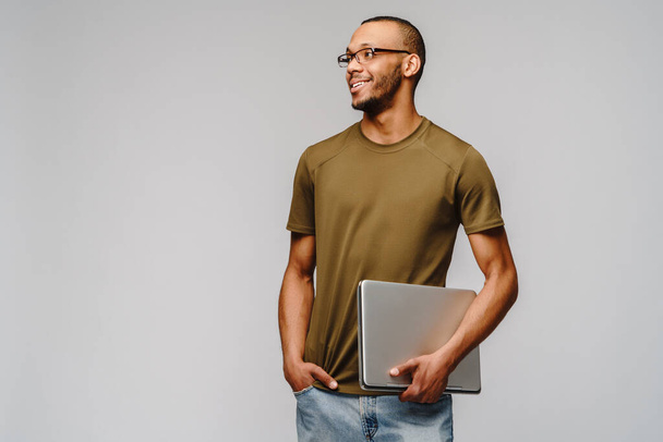 A young african american man wearing glasses holding laptop pc - Foto, afbeelding