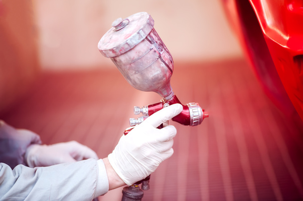 Worker painting a red car in paiting booth using professional tools and spray gun - Foto, Imagem