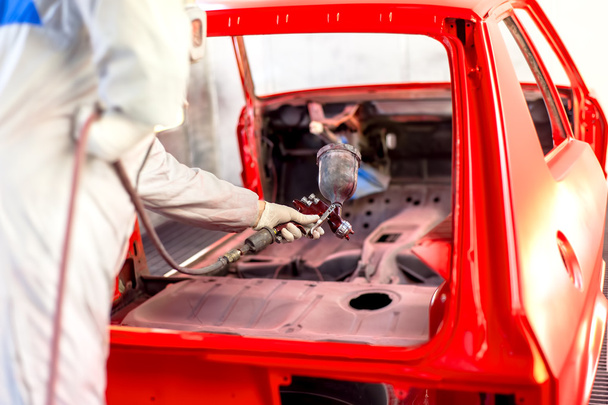 Worker painting a red car in a special garage, wearing a white costume - Foto, Imagem