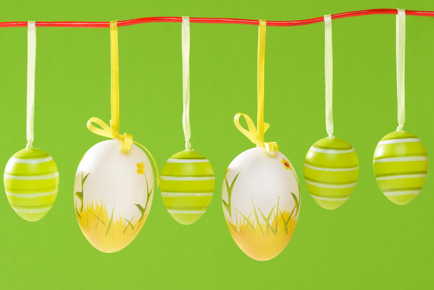 Huevos decorados con Pascua colgando de una cuerda roja sobre fondo verde
. - Foto, imagen