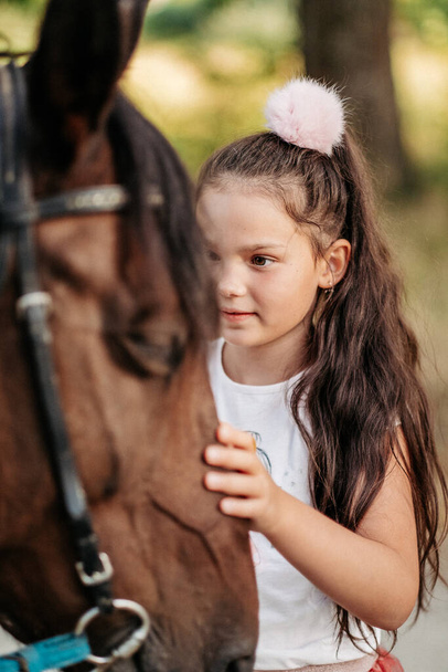 Przyjaźń dziecka z koniem. Mała dziewczynka pieszczotliwie głaszcze swojego konia. Spacerujące dziewczyny z koniem w parku jesienią. - Zdjęcie, obraz