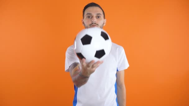 Young soccer player in white blue shirt holding soccer ball in his hands in front of camera with serious face - Imágenes, Vídeo