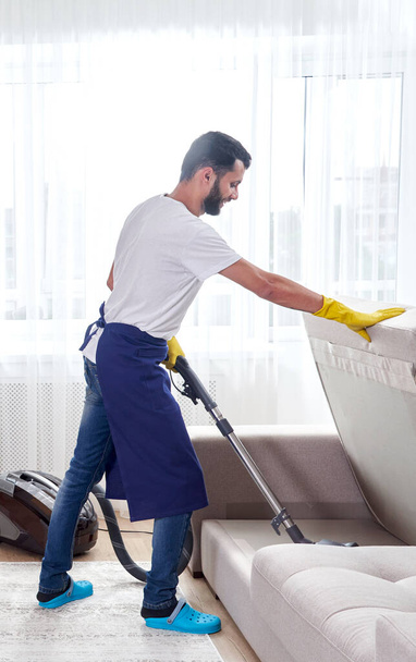 Jovem homem de limpeza sofá com aspirador de pó em deixar o quarto em casa - Foto, Imagem
