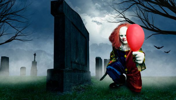 ένας κακός κλόουν με ένα μαχαίρι και ένα μπαλόνι σε ένα νεκροταφείο - Φωτογραφία, εικόνα