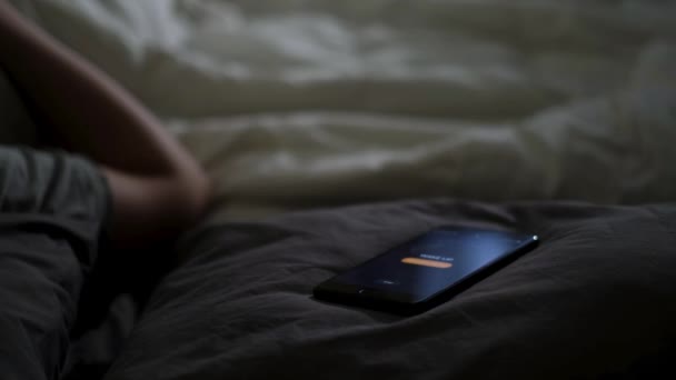 寝ている男がベッドの上に横になって電話で目を覚ました。コンセプト。朝早く家の毛布の上に横になる目覚まし時計をオフにしようとする男性の手. - 映像、動画