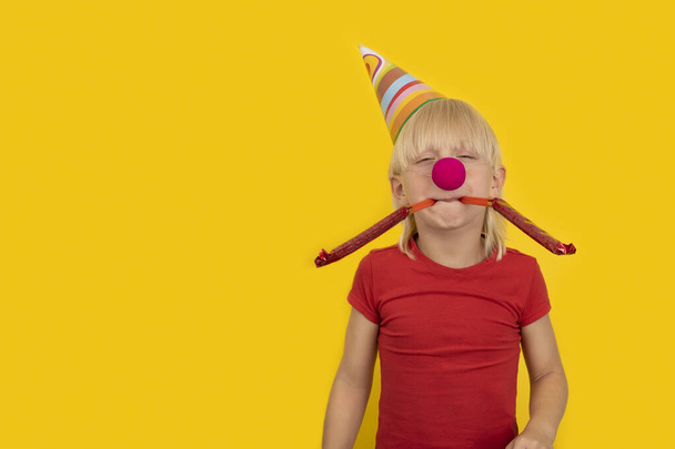 Junge bläst in festliche Pfeife. Porträt eines Kindes mit Clownsnase und Partyhut - Foto, Bild