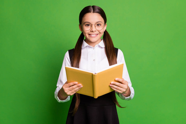Photo portrait of girl in spectacles holding yellow book with two hands isolated on vivid yellow colored background - Foto, Imagen