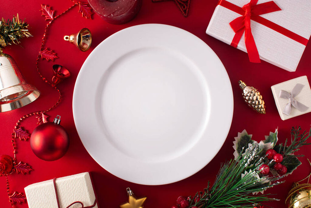 Boş beyaz tabak ve kırmızı arka planda Noel süsü. Noel yemeği konsepti. - Fotoğraf, Görsel