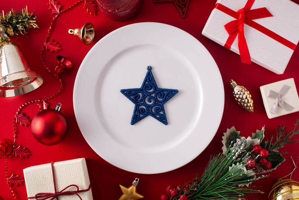 Assiette blanche avec étoile bleue et ornement de Noël sur fond rouge. Concept de dîner de Noël. - Photo, image