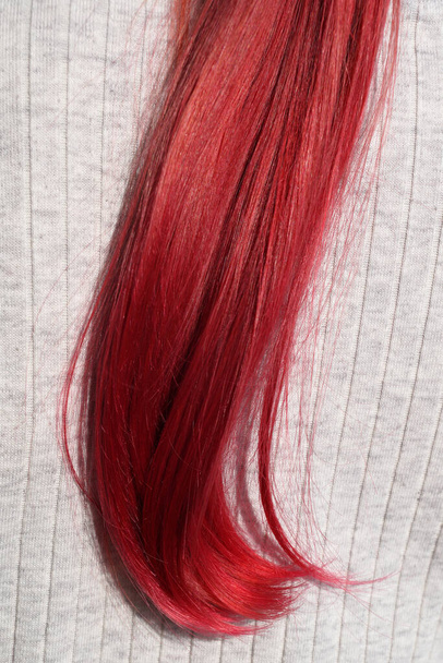 strand of dyed red female hair on a light background close-up - Photo, Image