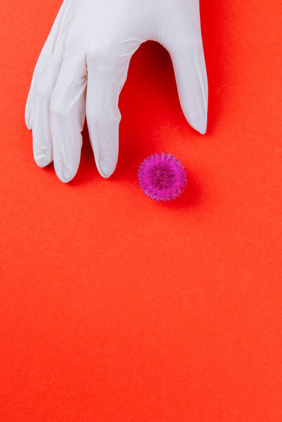 A hand in a white medical glove holds an abstract viral model of coronavirus on a red background. Protection against a pandemic virus. - Foto, imagen