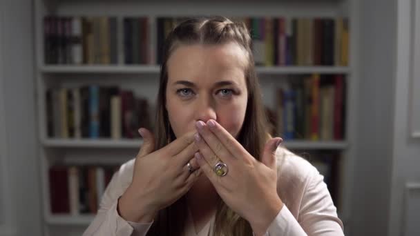 Γυναίκα κάθεται μπροστά από τη βιβλιοθήκη και κλείνει το στόμα της με τα χέρια - Πλάνα, βίντεο