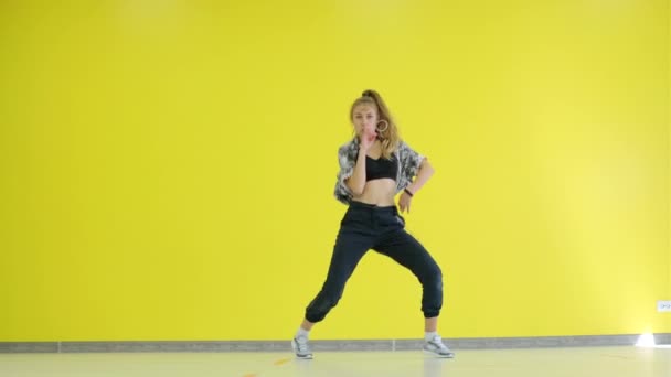 Jonge energieke vrouw dansend moderne jeugd dans vrije stijl in de studio tegen de achtergrond van een gele muur. geïsoleerd. - Video