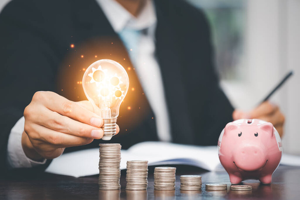 Рука бізнесмена тримає лампочку з лінією з'єднання і монети стоять на дерев'яному столі, збереження ідей та інвестиційного бюджету, концепція творчих ідей для економії грошей, копіювання простору
 - Фото, зображення