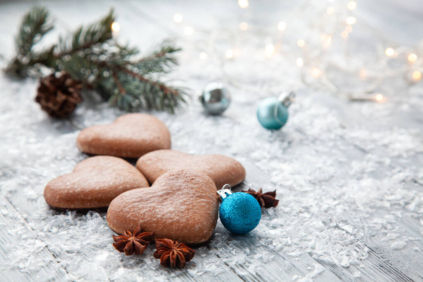 pan di zenzero di Natale sotto forma di un cuore e un ramo di albero di Natale con palline blu su uno sfondo di legno innevato - Foto, immagini