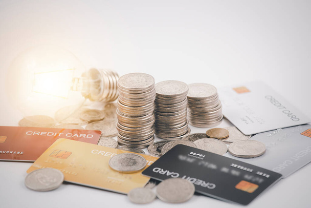Münzen mit Kreditkarte und Glühbirne auf weißem Hintergrund für Finanzen und Bankwesen, Sparen von Ideen und Investitionsbudget, Kreative Ideen zum Sparen - Foto, Bild