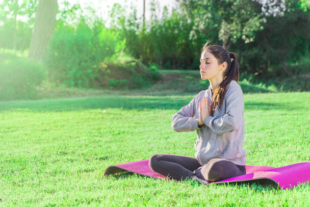 Young woman doing yoga in the morning in her garden with sunlight in lotus position, namaste, exercise, wearing sportswear.  - Foto, Imagem