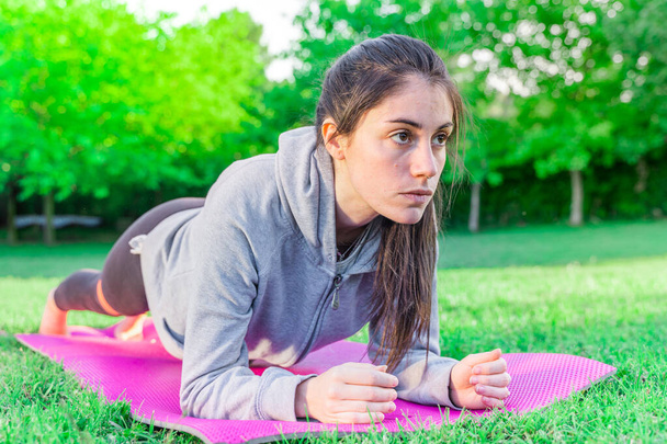 Young woman doing yoga in the morning in her garden with sunlight in lotus position, namaste, exercise, wearing sportswear and in plank strap pose. - Foto, Imagem