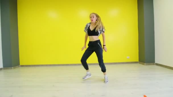 Jonge energieke vrouw dansen moderne jeugd dans gratis stijl in de studio tegen de achtergrond van een gele muur. - Video