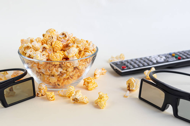 A transparent bowl of popcorn on a light surface. Nearby is a laptop, remote control and headphones. Home family watching movies. Copy space. - Photo, Image