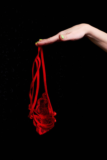 Erotic red panties in a female hand on a black background. - Фото, зображення