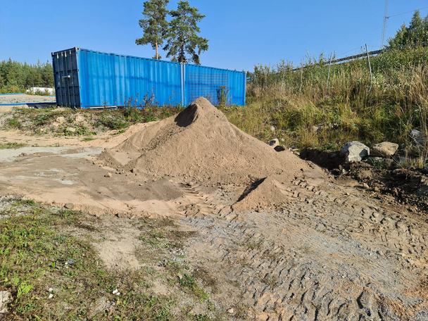 Vista natural del paisaje que muestra una pila de arena cerca de un gran contenedor azul. sobre fondo azul claro del cielo.  - Foto, Imagen