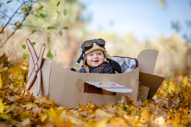 Uma criança feliz sonha em viajar em um avião e joga um piloto de avião. A criança senta-se em um avião de papelão e finge ser um piloto no parque no outono. - Foto, Imagem