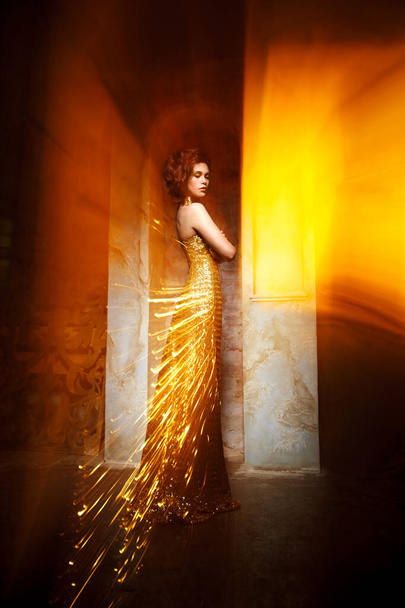 Beautiful elegant woman in a luminous dress with a train of sparks, mixed light. - Foto, afbeelding