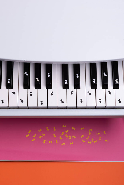 piano de juguete blanco con notas de papel. concepto de piano de música. vista desde arriba. Notas de música blanca, negra y amarilla. - Foto, Imagen