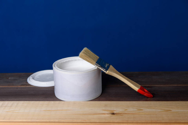 A can of white paint and a paintbrush on a wooden table. - Foto, Bild
