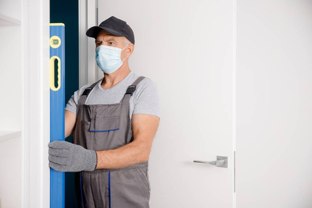 Ξυλουργός σε ιατρική μάσκα διαδικασία εγκατάστασης πόρτα ξύλο - Φωτογραφία, εικόνα