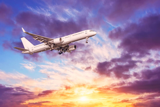 Samolot lecący na niebie, niedaleko lotniska. Piękne, żywe niebo zachód słońca z chmurami różnych poziomów wysokości różne odcienie podświetlone przez światło słoneczne - Zdjęcie, obraz