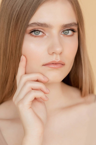 Belleza cuidado cara concepto de moda. Retrato vertical de hermosa joven rubia con la piel limpia, fondo beige - Foto, Imagen