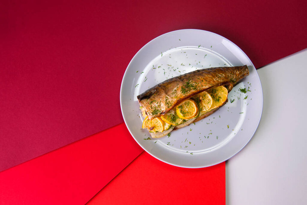 Top view of baked mackerel with lemon slices and onion on gray plate on colorful red background. Grilled fish served with fresh herb dill. - Zdjęcie, obraz