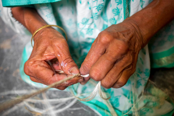 Uma mulher de idade está fazendo em suas mãos magras uma corda da fibra da bananeira em Madhupur, Tangail, Bangladesh. - Foto, Imagem