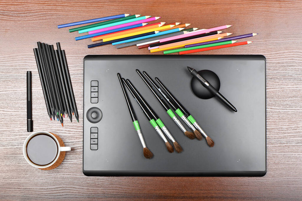 Top view professional graphics tablet with paintbrushes, digitized and multicolored pens. Isolated on wooden background. High resolution photo. Full depth of field. Table concept for work. - Photo, Image