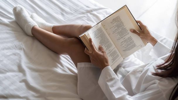 Azjatka czyta książkę na łóżku po wstaniu rano z miękkim rankiem. Poranna koncepcja stylu życia. - Zdjęcie, obraz
