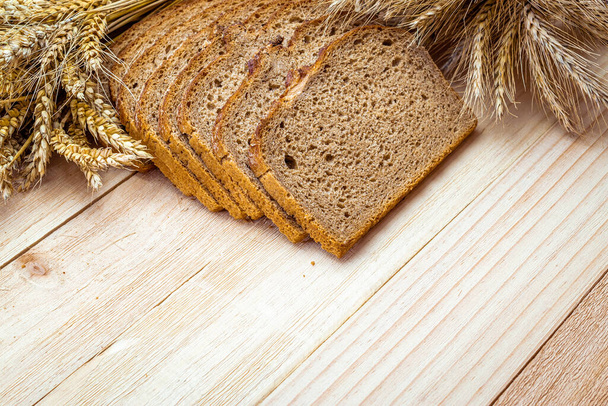Žitný chleba. Pekárna s křupavými bochníky a drobky. Čerstvý bochník rustikálního tradičního chleba s pšeničným uchem nebo žitným bodcem na přírodním dřevěném pozadí. Zdravé potraviny koncept - Fotografie, Obrázek