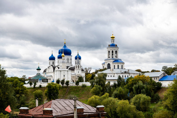 old white monastery with blue domes on the background of green trees and the river - Photo, Image