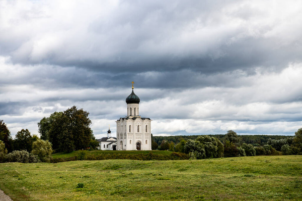 snow-white stone old church against the background of a green meadow and lake before a summer thunderstorm - Foto, imagen