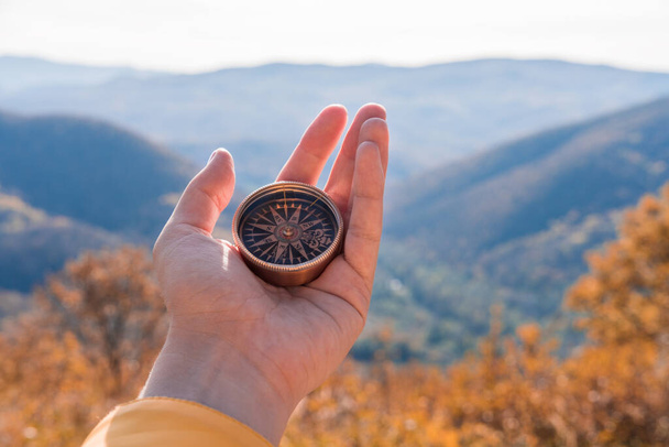 Kobieta ręka podróżnika, turysta z kompasem na tle jesienny krajobraz lasu z górami na horyzoncie w pomarańczowych kolorach jesienią. - Zdjęcie, obraz