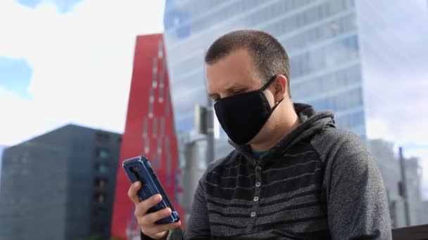 Mann mit Smartphone mit Maske auf Bank - Filmmaterial, Video